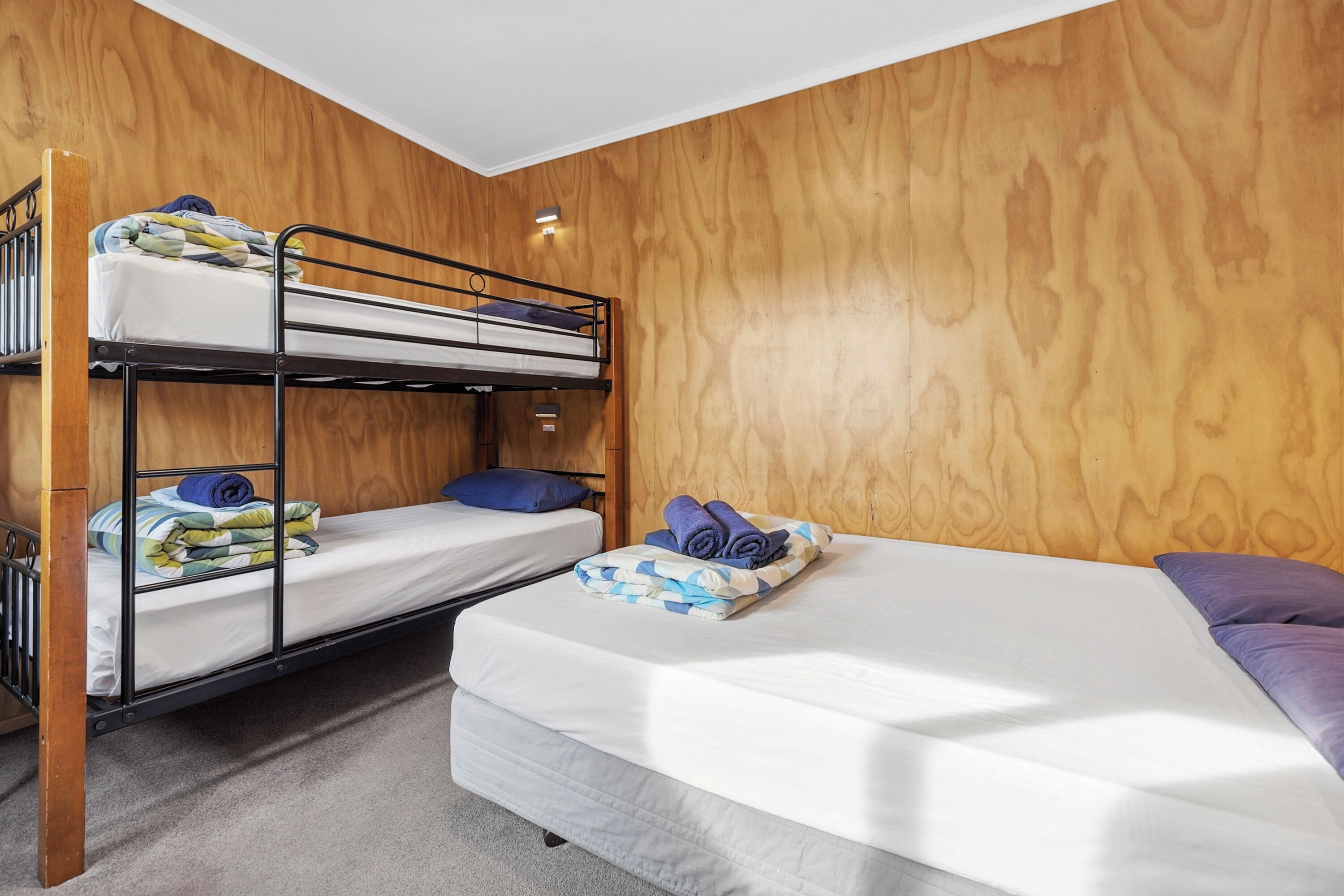 A bunk bed room with a wooden wall, a single bed, and a nightstand.