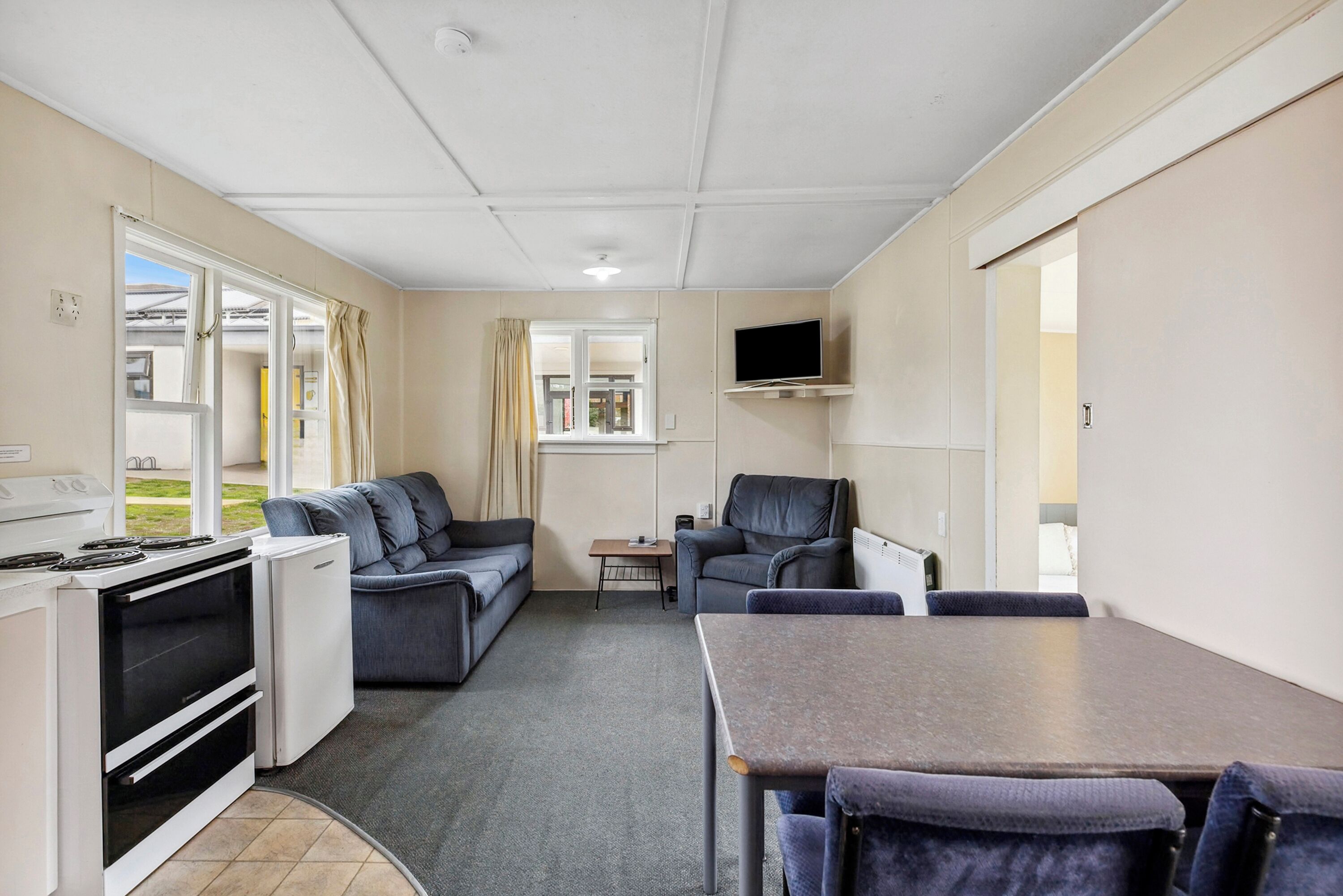 A compact room with a kitchenette, a sofa, a dining table, and a TV mounted on the wall.