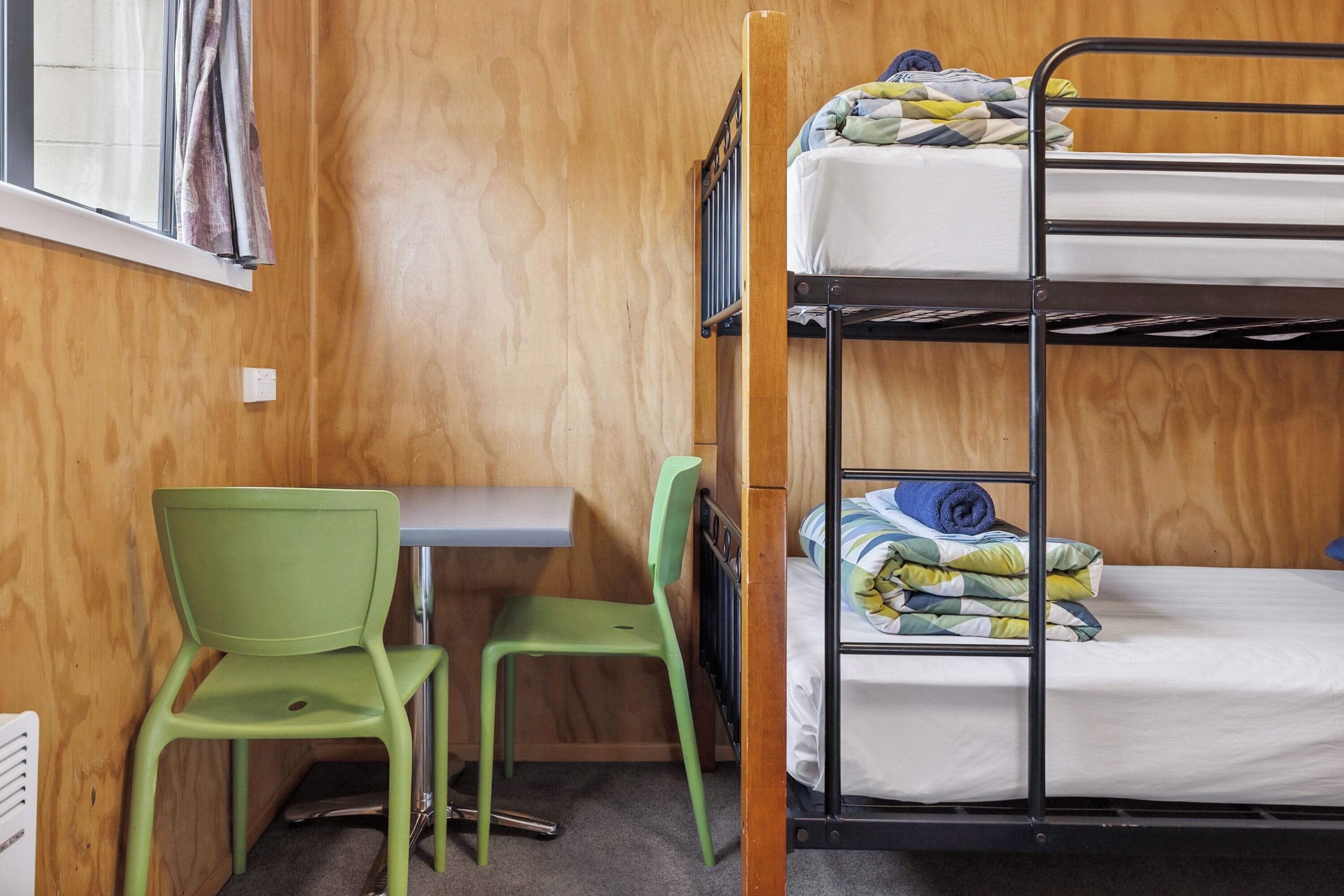 A bunk bed with a lower bunk, a desk with a chair, and a window with curtains.