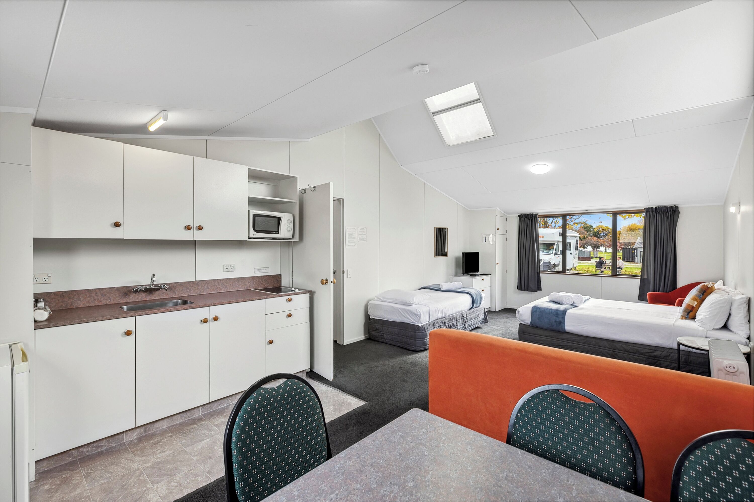 A compact hotel room with a kitchenette, a bed, a sofa, and a dining area.