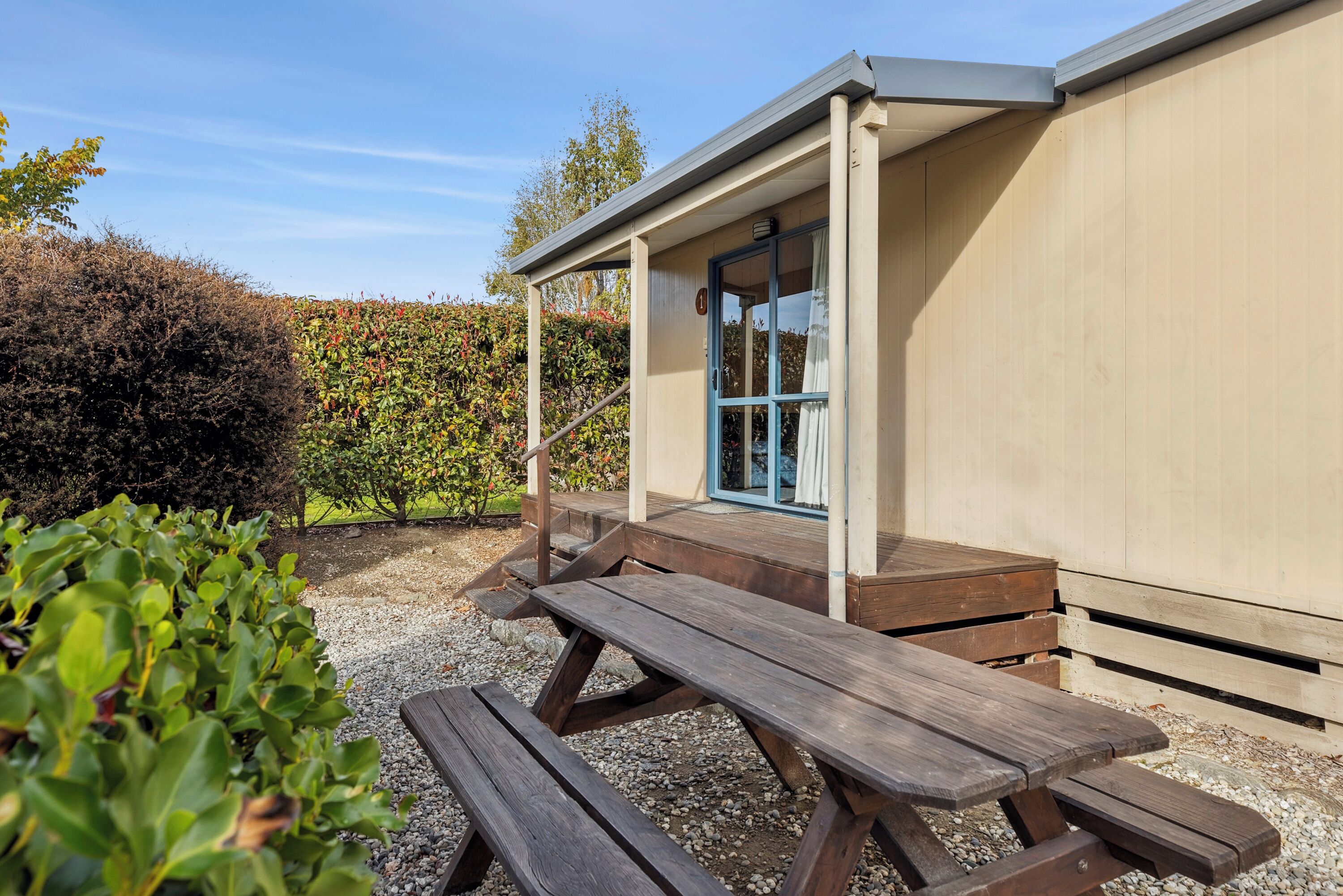 A wooden picnic table outside a building with a covered porch and a door with blue trim.