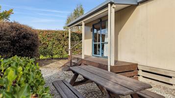 A wooden picnic table outside a building with a covered porch and a door with blue trim.