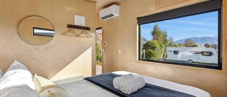A modern bedroom with a large window, a round mirror, and a neatly made bed.