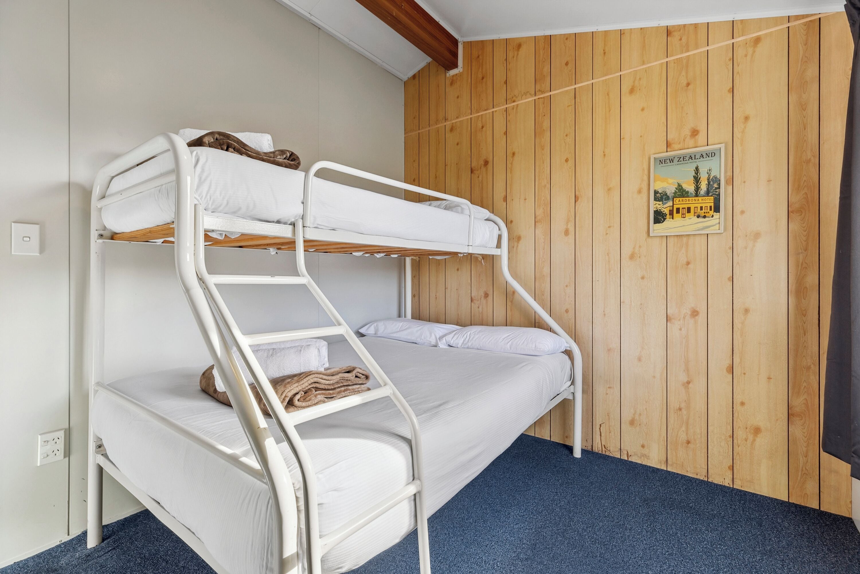 A bunk bed room with wooden panel walls, a poster of New Zealand, and a blue carpet.