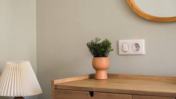 A wooden bedside table with a lamp, a small potted plant, and a wall socket.