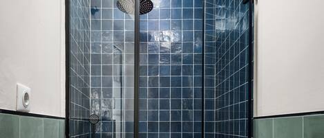 Ducha con cerramiento de vidrio, azulejos azules y suelo a cuadros verde y blanco.