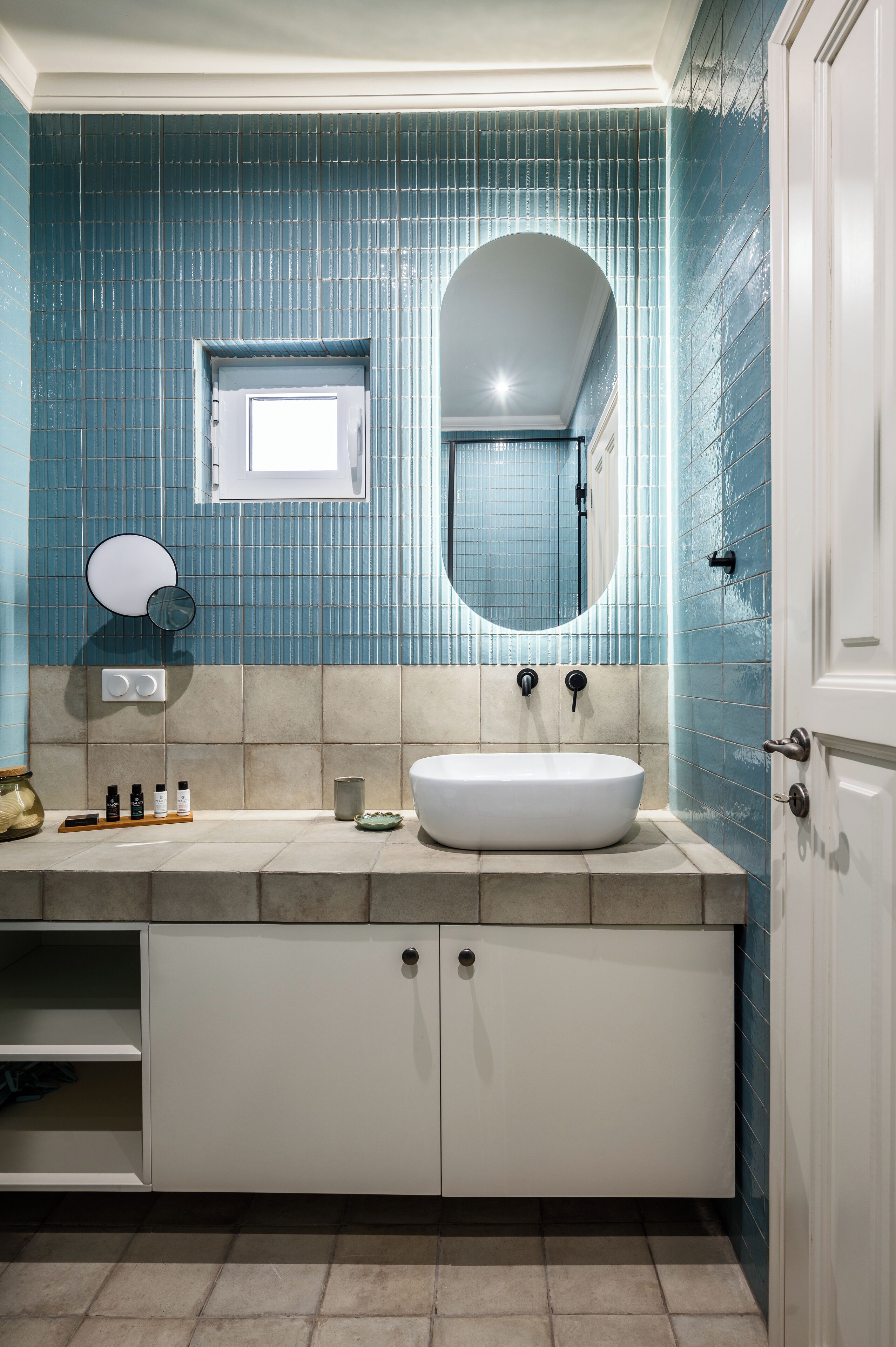 Une salle de bain avec des murs recouverts de carreaux bleus, un lavabo blanc et un miroir.