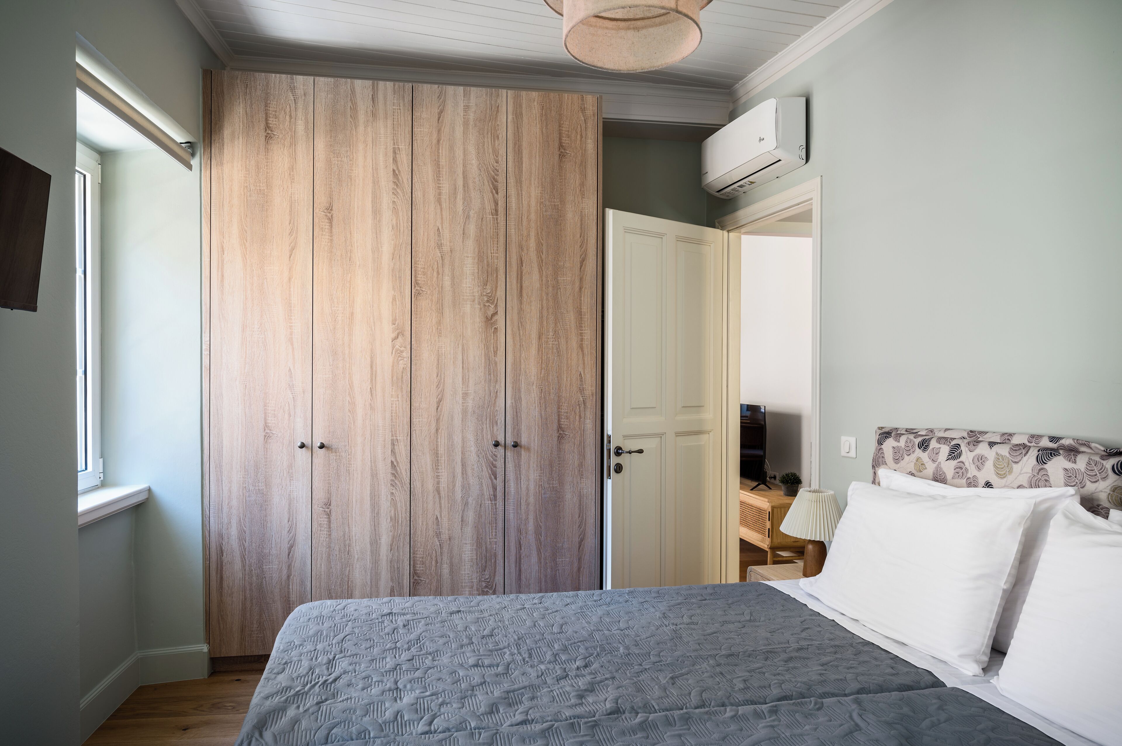 Une chambre avec une grande armoire en bois, un lit avec une literie blanche et un petit bureau avec une lampe.