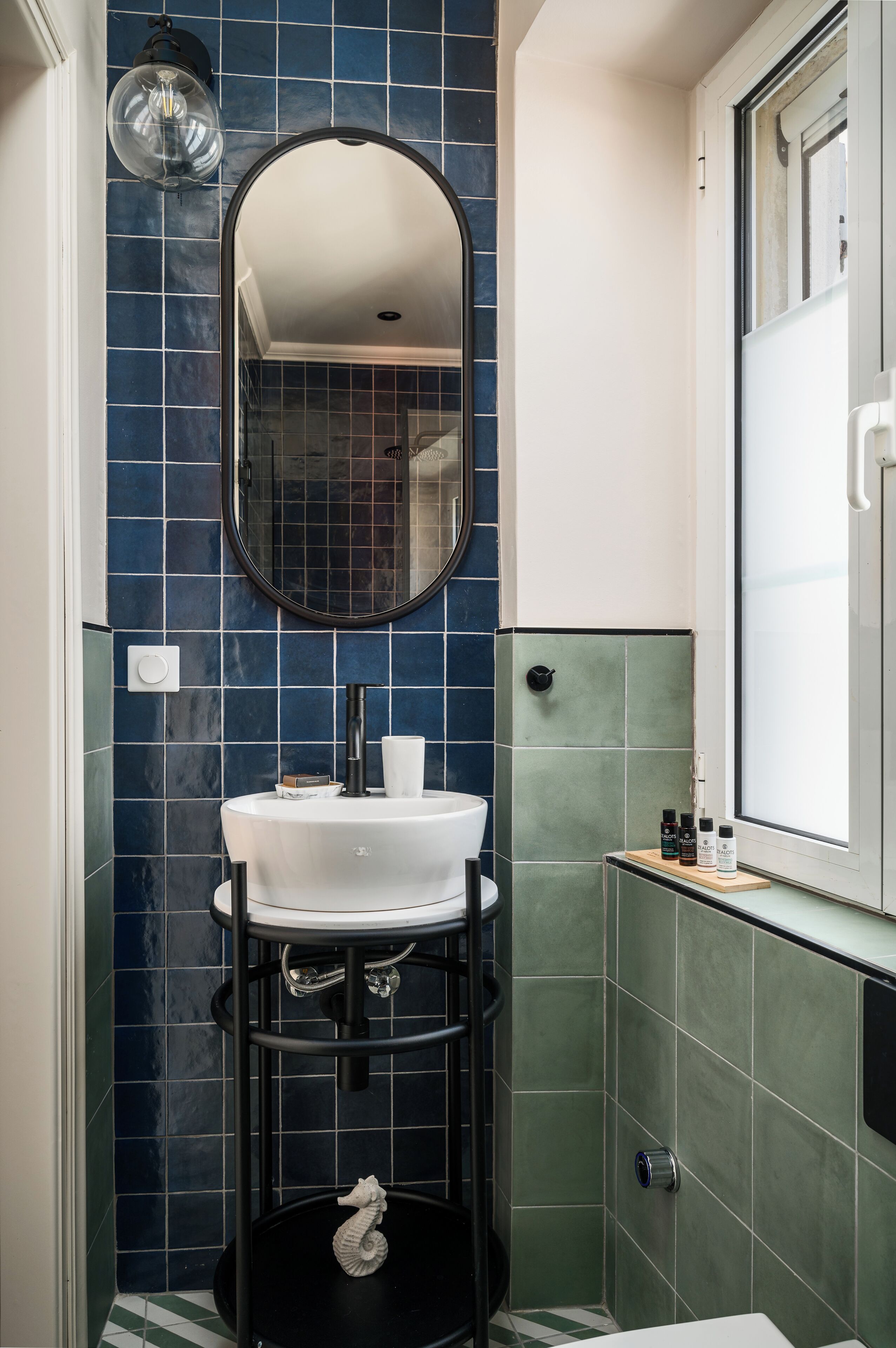 Een badkamer met een witte wastafel, een ronde spiegel en een zwart voetstuk.