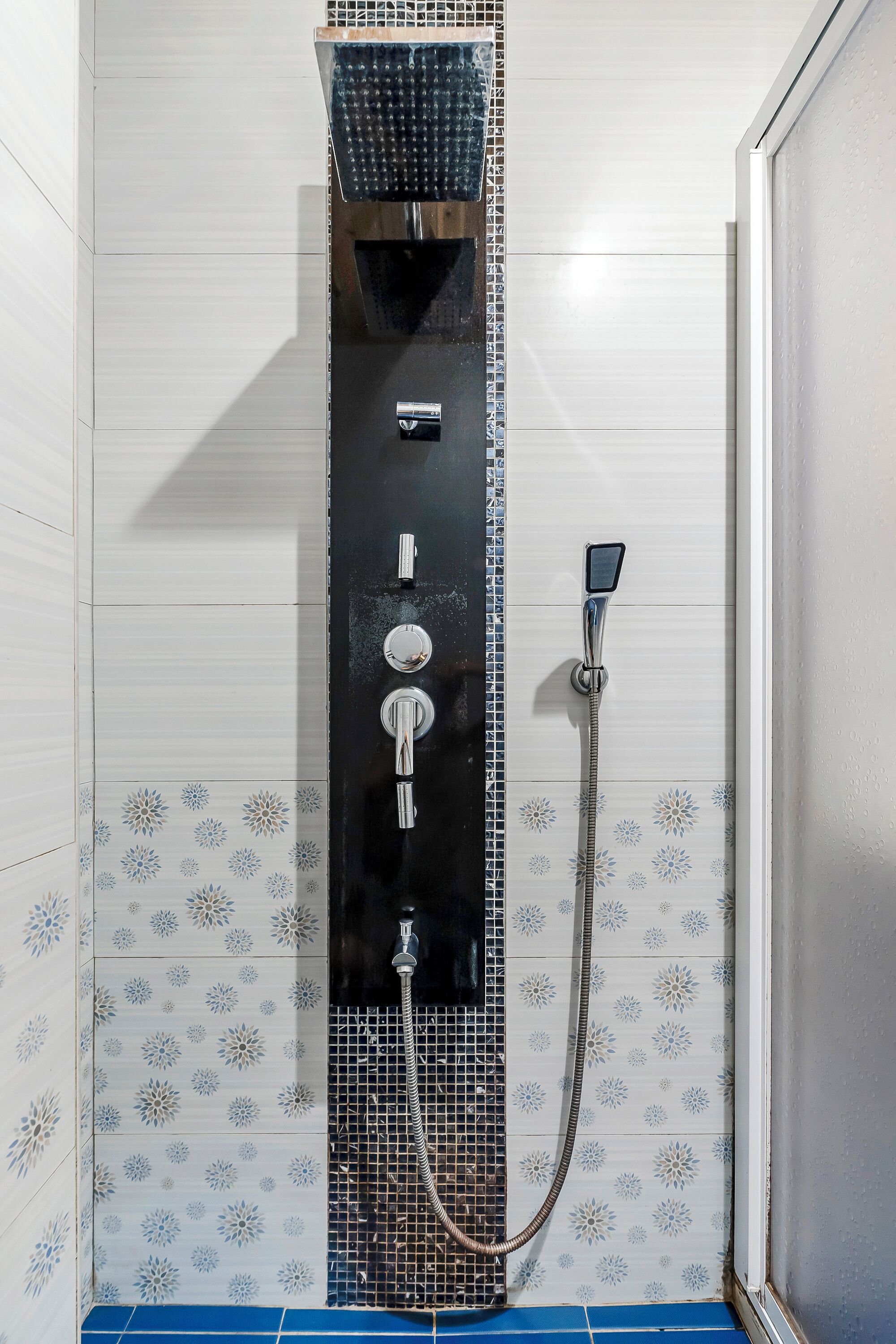 Un baño con ducha vertical, paredes de azulejos y suelo azul.