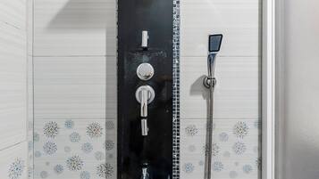 Un baño con ducha vertical, paredes de azulejos y suelo azul.