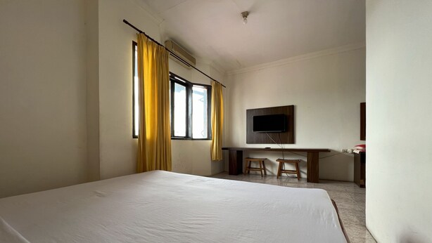A hotel room with a large bed, a desk with two chairs, a television on the wall, and a window with curtains. - Hotel O Kos Rian (Pallangga)