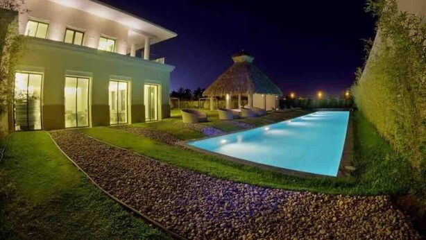 Ein modernes Haus mit Schwimmbad, einem Reetdachhaus und einem gepflegten Rasen.