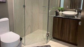Ein modernes Badezimmer mit einer gläsernen Dusche, einer weißen Toilette und einem Holzbadezimmerhocker mit Waschbecken.