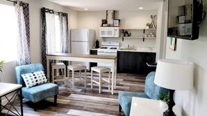 Un espace de vie compact comprenant un coin cuisine, un coin repas et un espace détente avec un canapé et des fauteuils.
