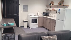 A compact living space with a kitchenette, a sofa, a small table, and a door. - 2 Bedroom along Highway 71<br>This suite is on the 2nd level and requires guests to use stairs. (Arnolds Park)