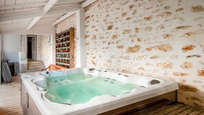 A wooden deck leading to a spa area with a hot tub, a stone wall, and a wooden shelf with bottles. - 18th century residence with Jacuzzi near Paris (Mennecy)