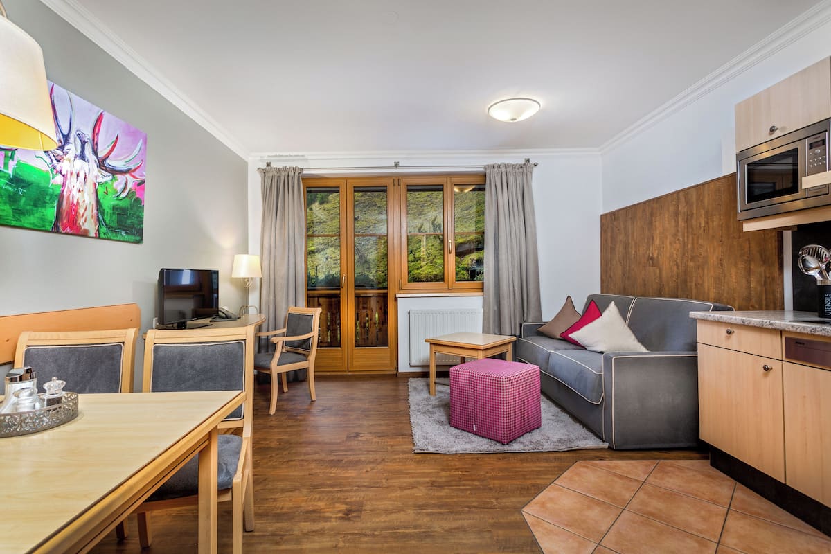 A compact living space with a dining area, a sofa, a television, and a kitchen area with a microwave.