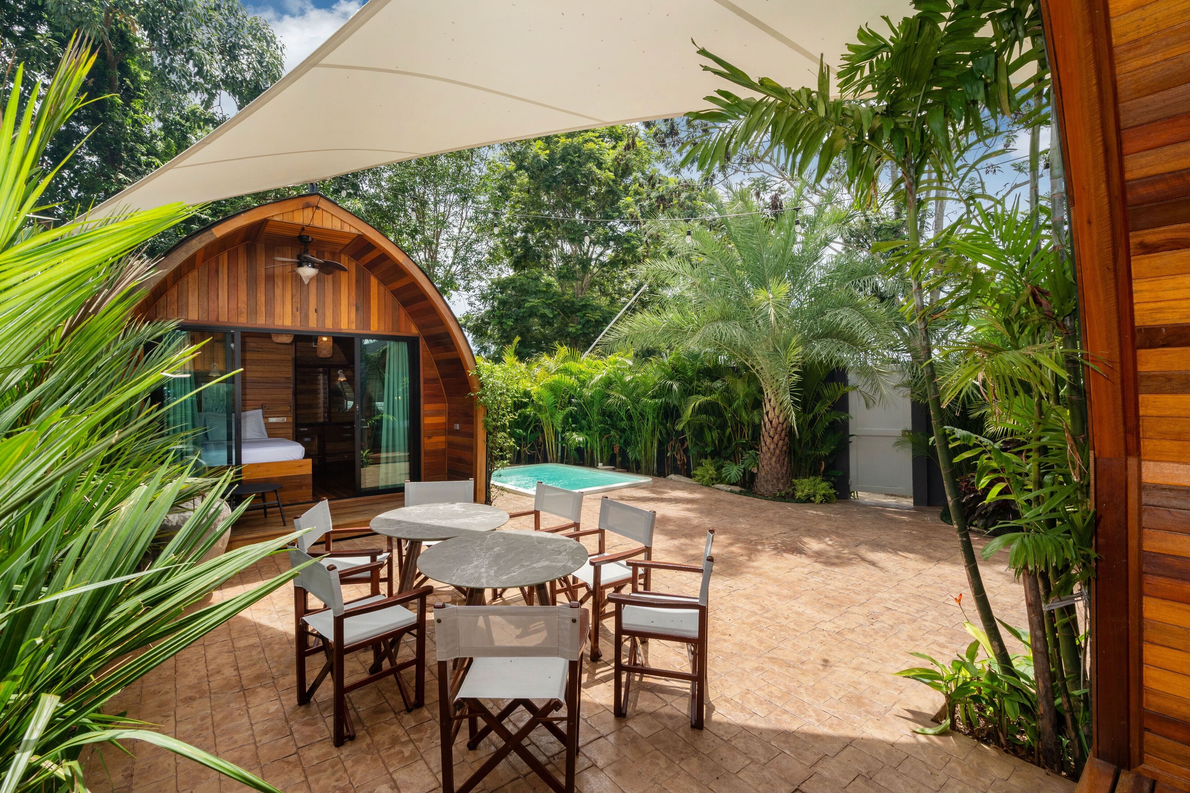 A wooden cabin with a glass door, a pool, and a patio with outdoor furniture.