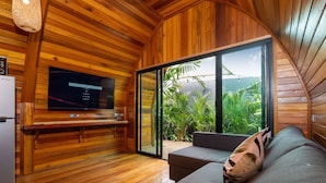 Ein Holzinterieur mit Fernseher, Sofa und einer Glastür zum Garten.