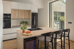 A modern kitchen with a central island, bar stools, and a view through a large window. - Luxury Villa Casa Maria with pool (Tar)