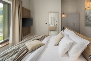 A modern bedroom with a bed, a television mounted on the wall, a wardrobe, and a bathroom visible through a doorway. - Luxury Villa Casa Maria with pool (Tar)