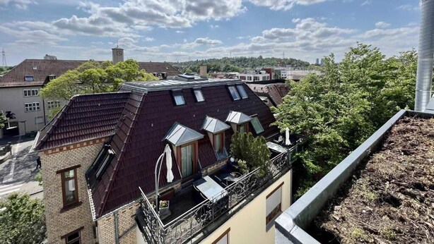 Un immeuble résidentiel à plusieurs niveaux, doté d’une cheminée bien visible et surplombant un ciel dégagé parsemé de nuages.