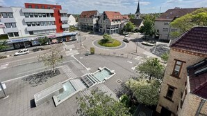 Une place de ville avec un rond-point, des bâtiments et le clocher d’une église.