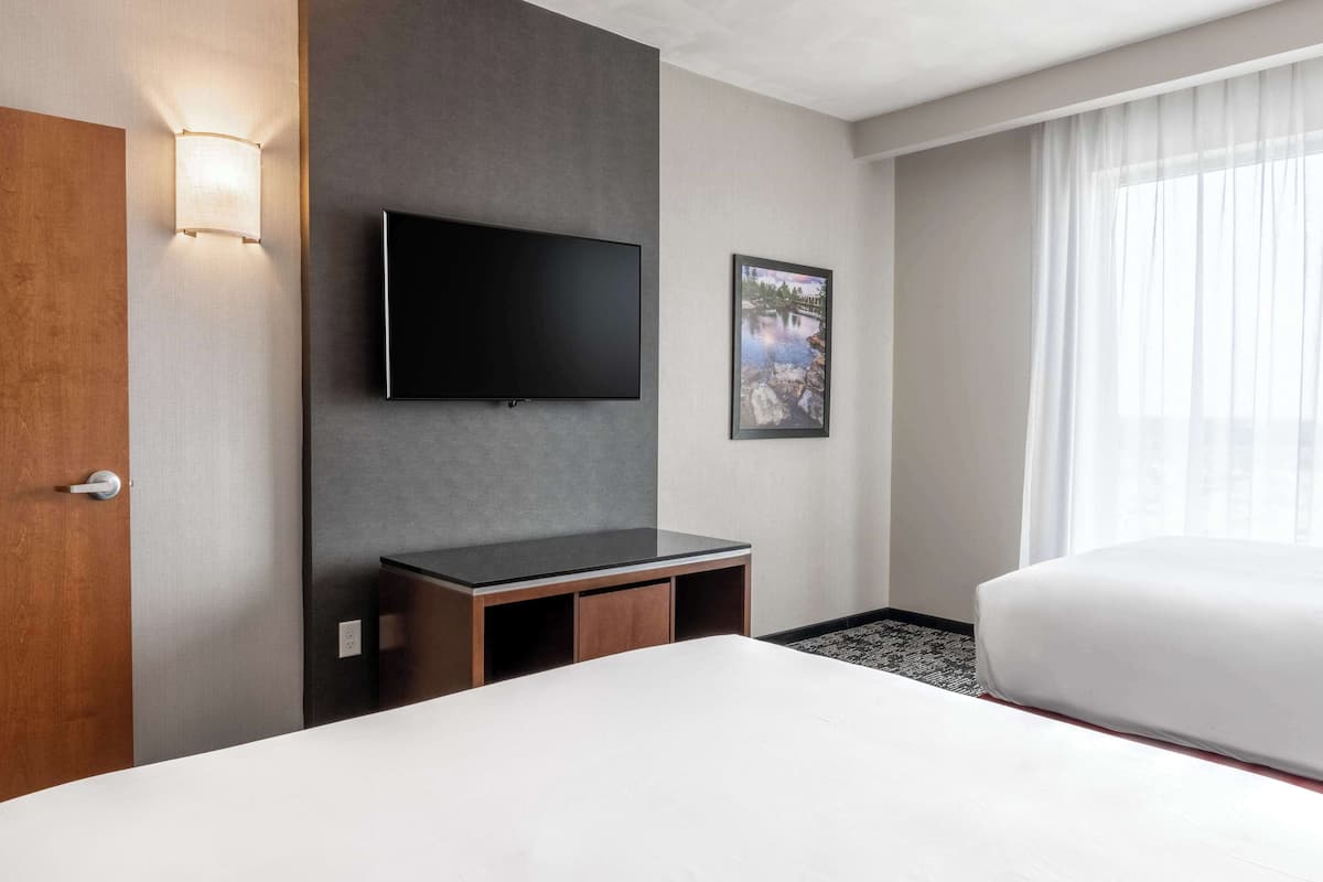 Quarto de hotel com televisão de tela plana na parede, uma cama, uma pequena mesa de madeira e um quadro na parede.