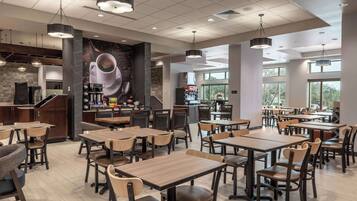 A modern cafe with multiple tables and chairs, a coffee bar, and large windows allowing natural light.