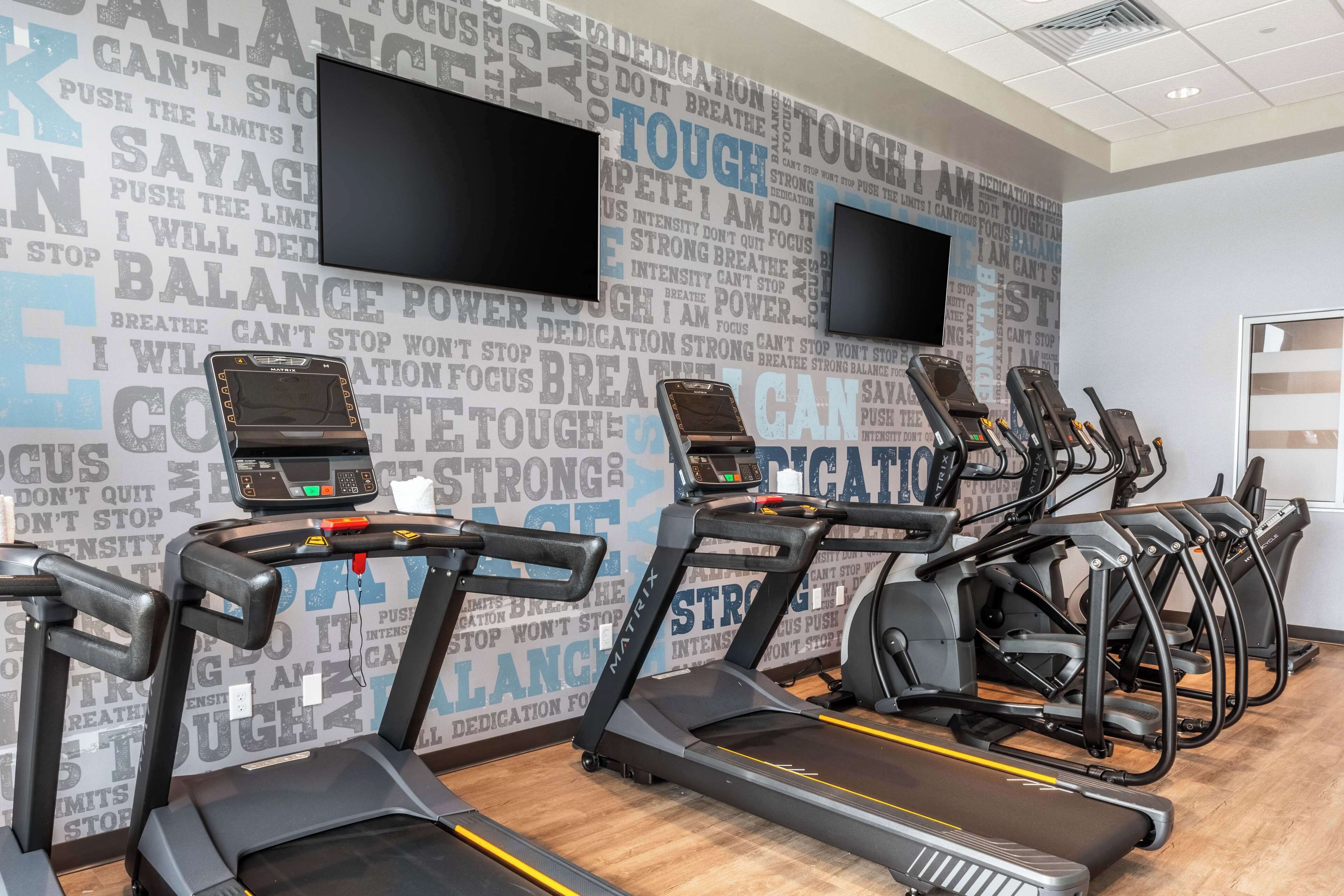 A gym with treadmills and stationary bikes, motivational wall art, and a flat-screen TV.