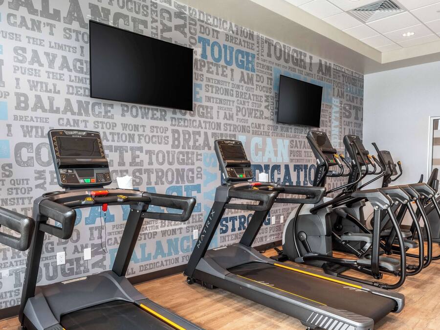 A gym with treadmills and stationary bikes, motivational wall art, and a flat-screen TV.