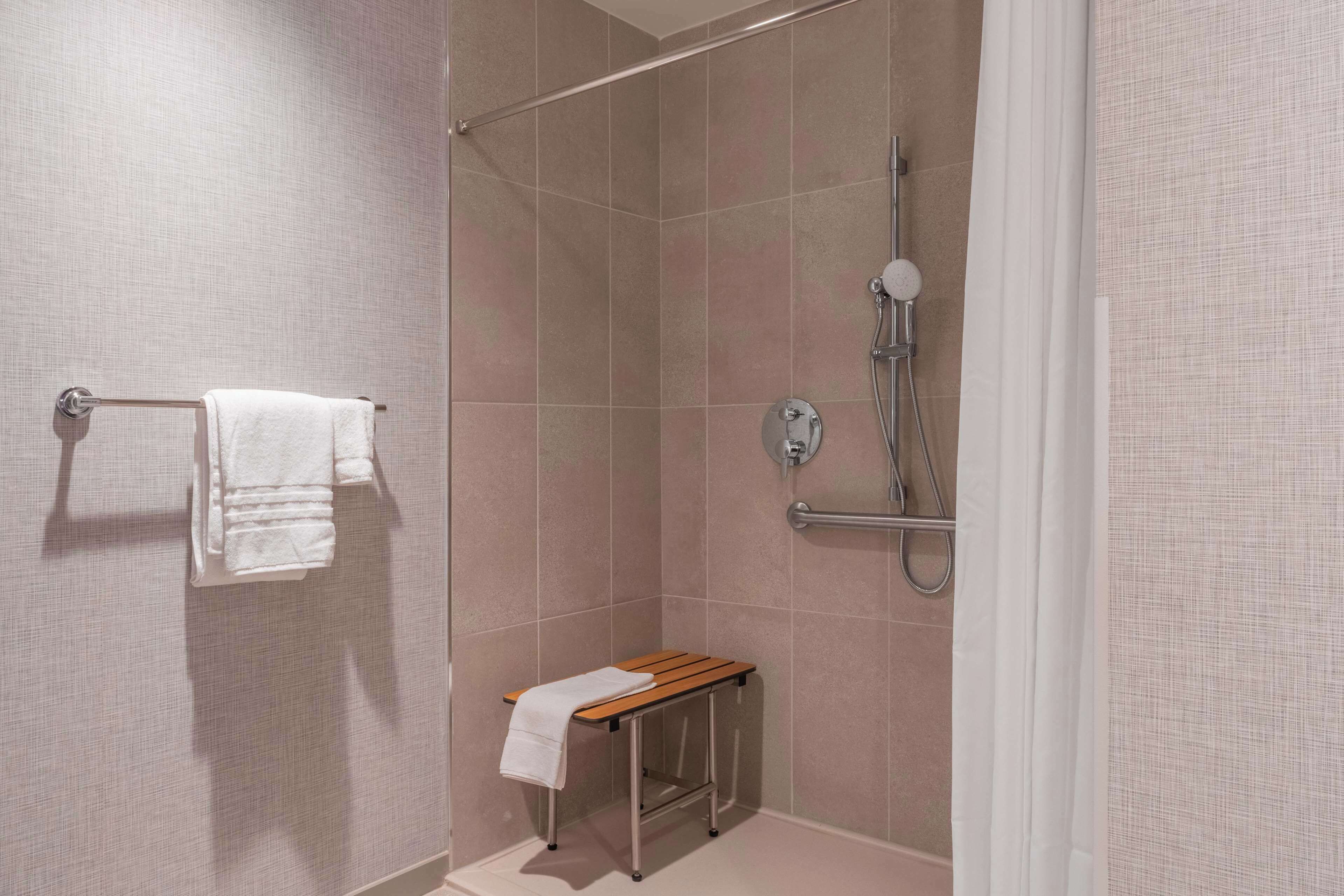 A modern bathroom with a shower, a towel rack, and a bench.