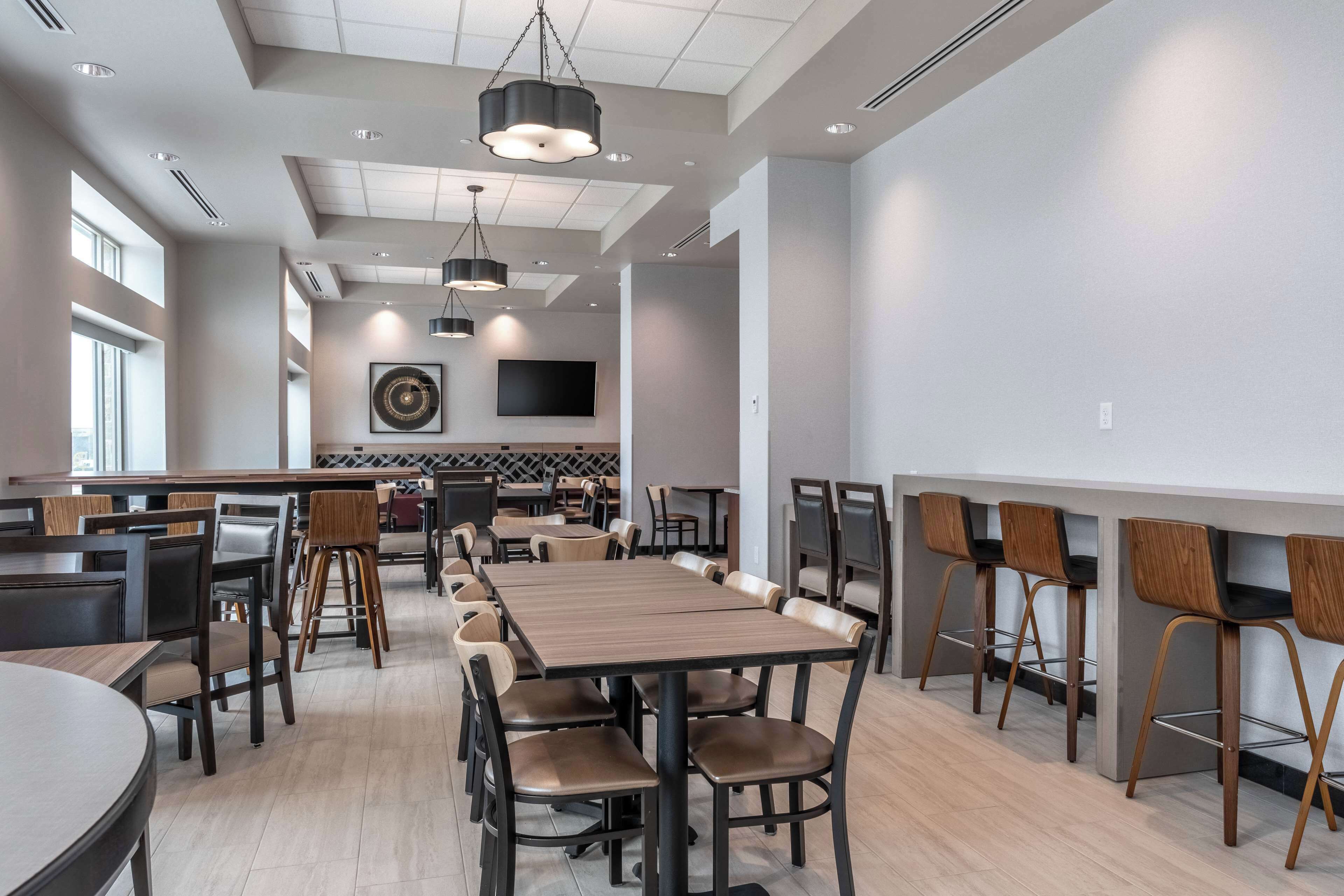 A modern dining area with high tables and chairs, recessed lighting, and a large wall-mounted TV.