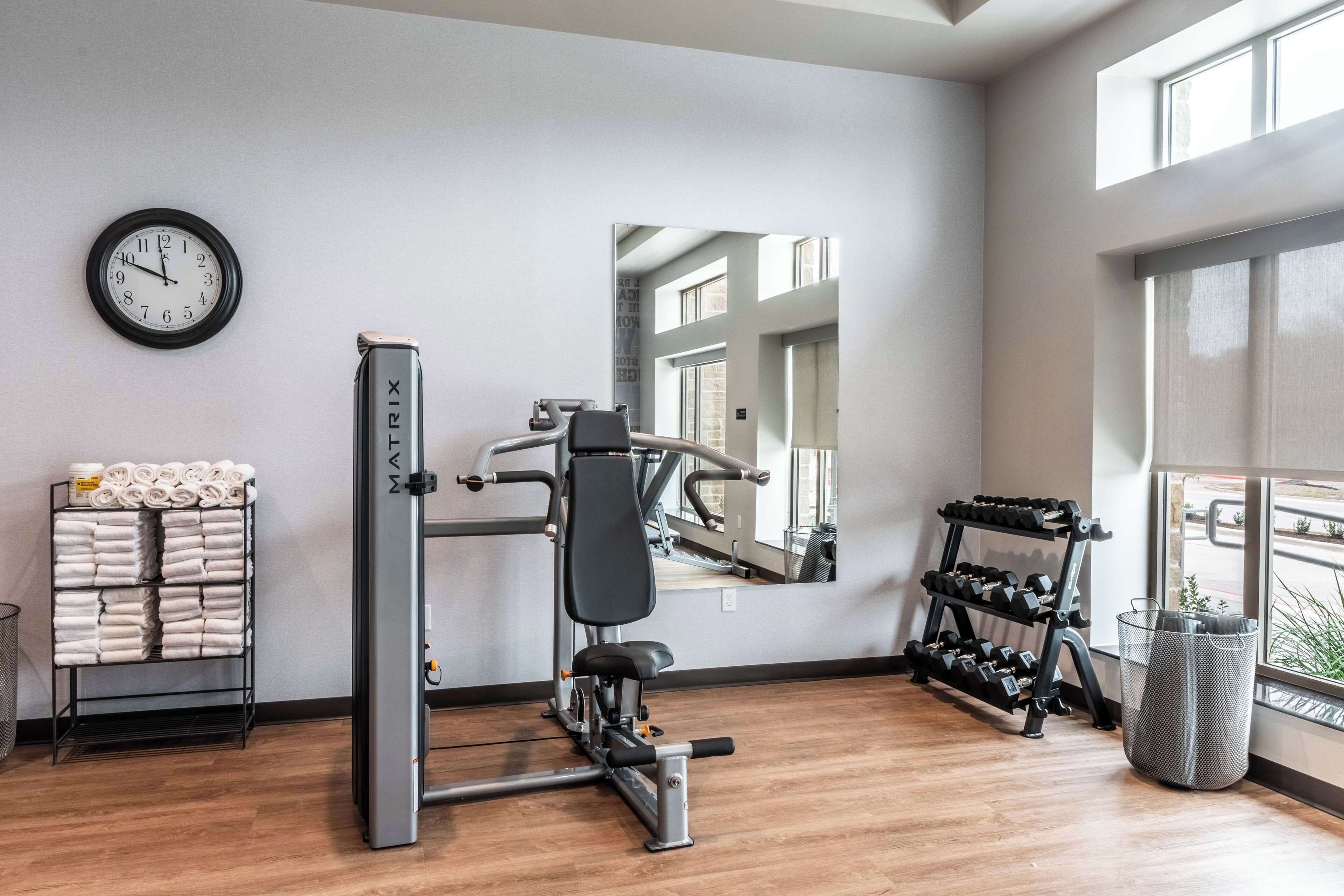 Ein Fitnessraum mit Wanduhr, Trainingsgeräten, einer Hantelbank und einem Fenster mit Blick.