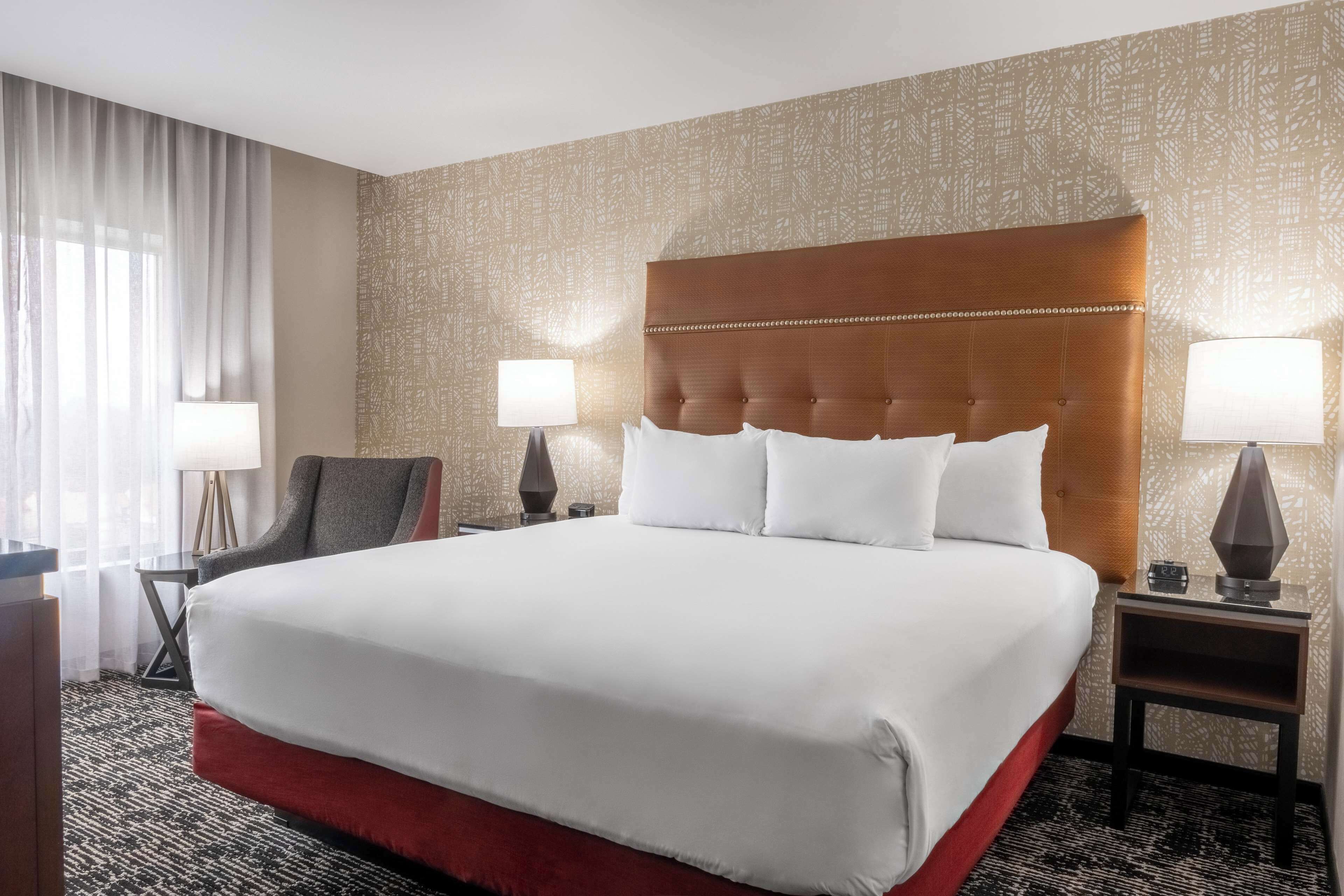 A hotel room with a large bed, two bedside tables, a chair, and a window with curtains.