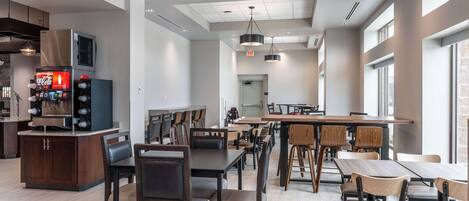 Un restaurant moderne avec des tables et des chaises en bois, un coin bar et de grandes fenêtres qui laissent entrer la lumière naturelle.