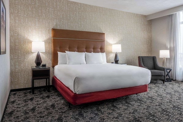 A hotel room with a large bed, two bedside tables with lamps, a red upholstered chair, and patterned wallpaper. - Drury Plaza Hotel College Station (College Station)