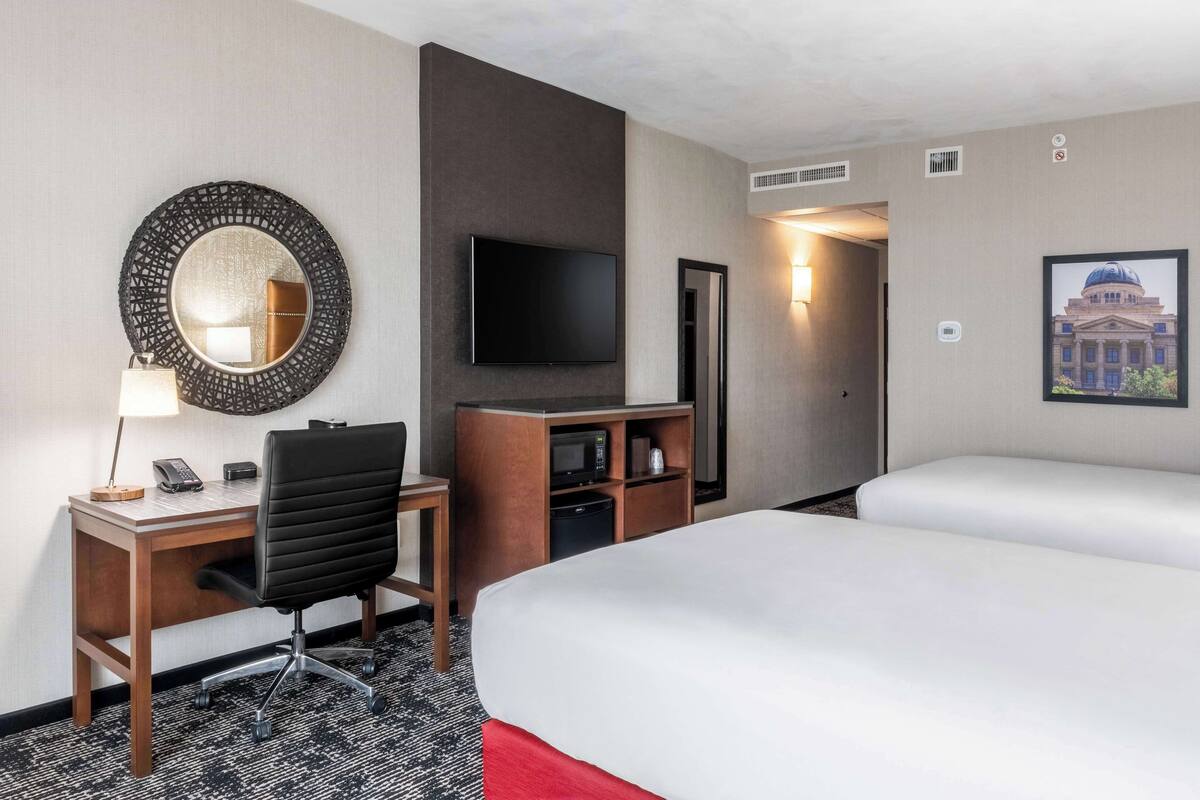 Quarto de hotel com escrivaninha, cadeira, televisão e duas camas.