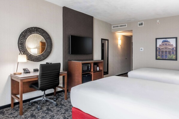 A hotel room with a desk, chair, television, and two beds.