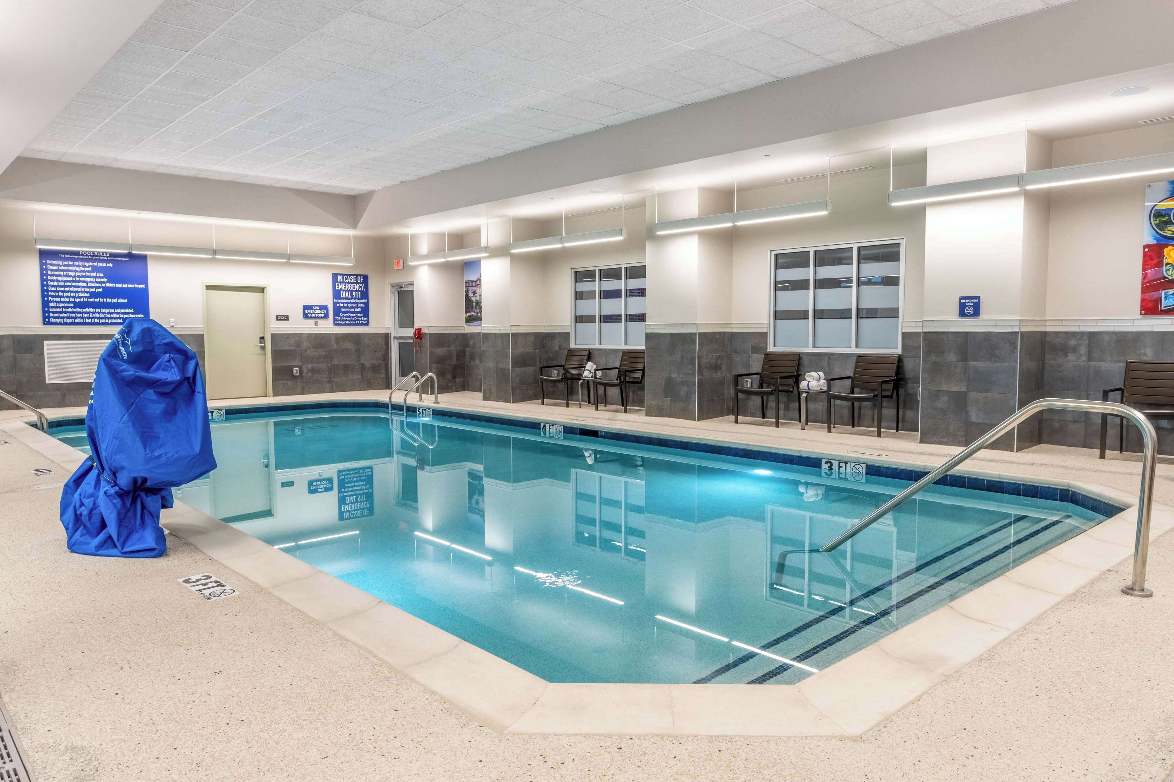 Un espace piscine doté d’une piscine à eau claire, de sièges disposés le long des bords et d’une zone couverte avec un auvent bleu.