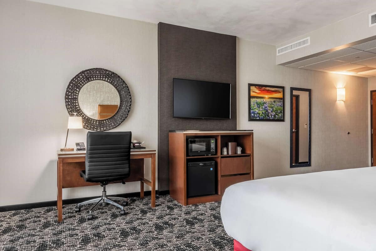 Quarto de hotel com cama, escrivaninha com cadeira, televisão, micro-ondas e pequeno frigorífico.