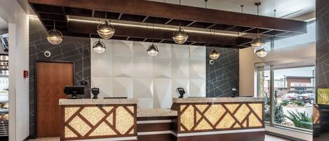 A reception area with a modern design, featuring a geometric wall pattern, a wooden reception desk, and pendant lighting.