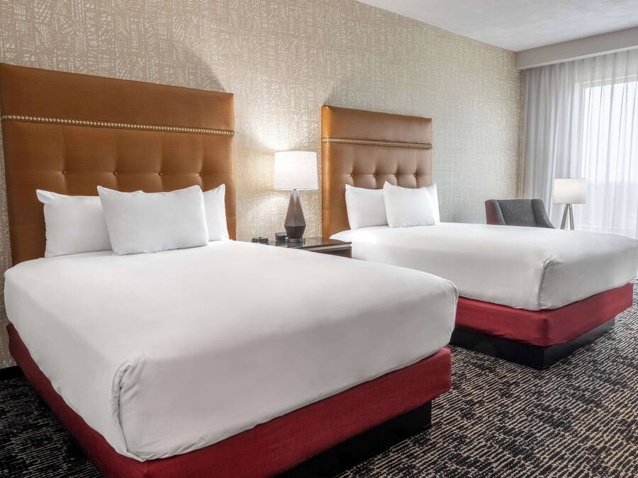 A hotel room with two beds, each with a headboard and bedside tables.
