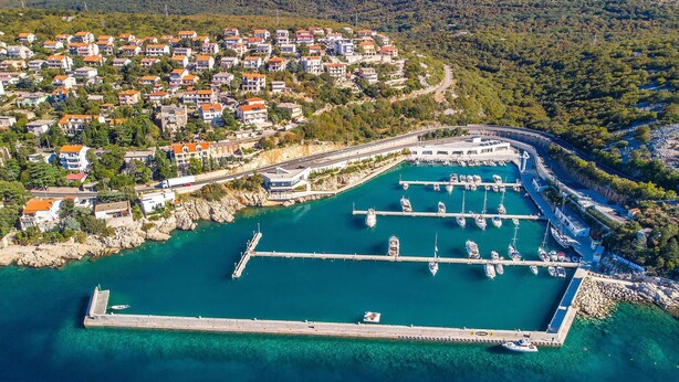 Vue aérienne d’une ville côtière avec un port de plaisance, des immeubles résidentiels et une côte rocheuse.