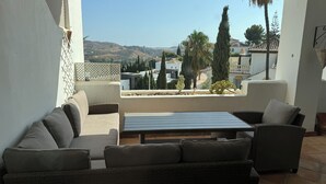 A patio with wicker furniture and a view of a hilly landscape.