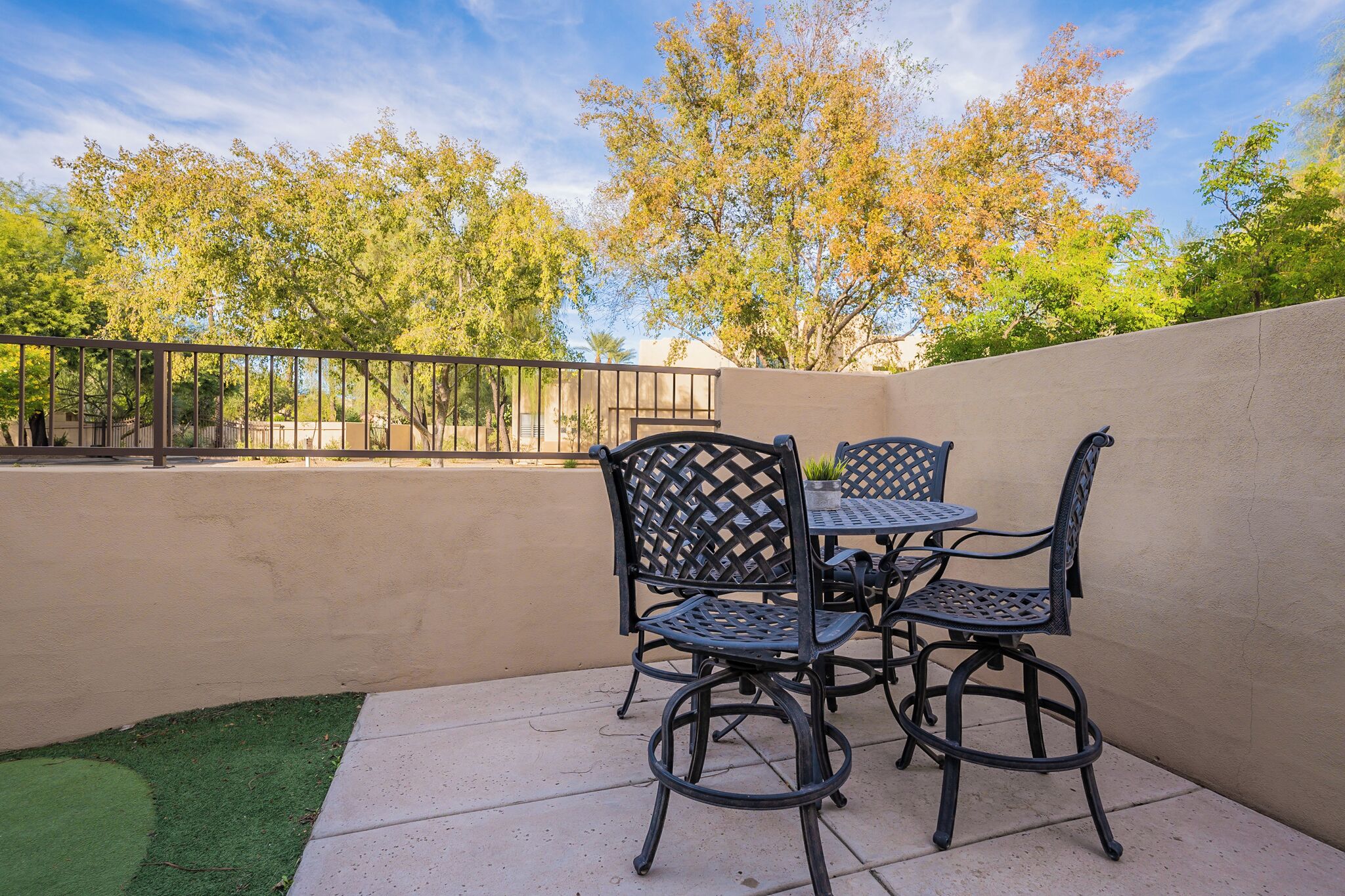 Une terrasse extérieure avec une table et des chaises, entourée d’un petit muret et d’arbres.