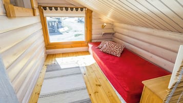 A cozy log cabin room with a red bed, a window with a view of the outside, and a wooden ceiling.