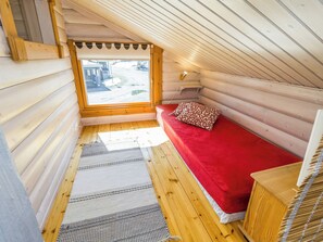 A cozy log cabin room with a red bed, a window with a view of the outside, and a wooden ceiling.