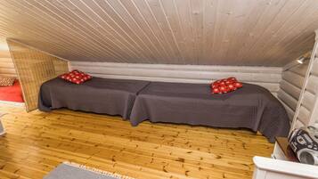 A small, cozy room with a sloped ceiling and wooden walls. There are two beds with matching bedding and pillows.